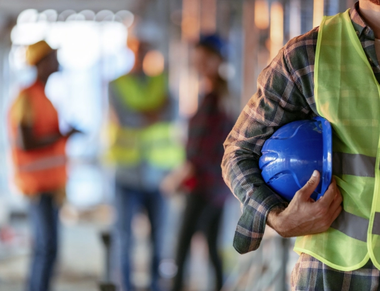 Pracownik w stroju roboczym trzymający niebieski kask ochronny